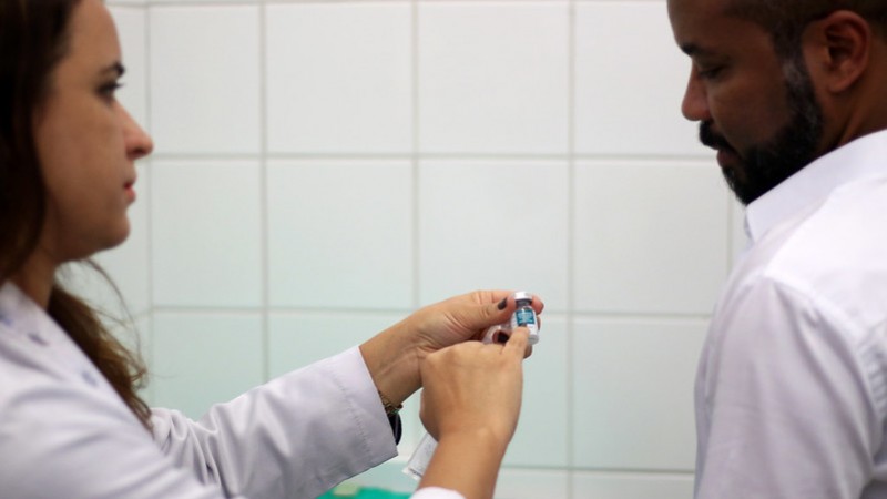 Uma profissional de saúde mostra o frasco de vacina para um homem. 