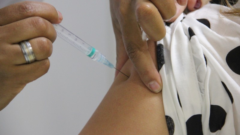 Imagem mostra o momento da vacina. Uma profissional de saúde vacina o braço de uma mulher. 