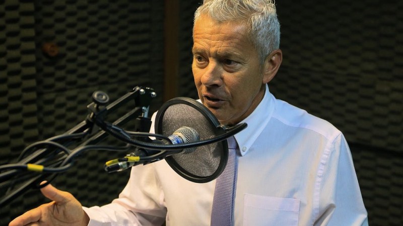 Secretário João Gabbardo, sentado, fala em frente ao microfone num estúdio de rádio.