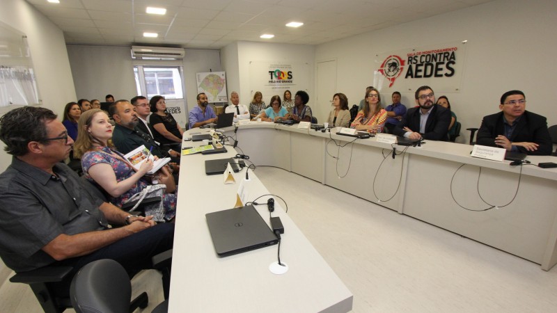 Participantes da reunião, sentados em torno de uma mesa em formato de U, ouvem o secretário Gabbardo falar.  