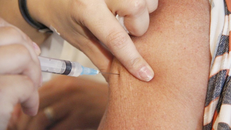Imagem mostra um braço tomando vacina de uma profissional de saúde. 