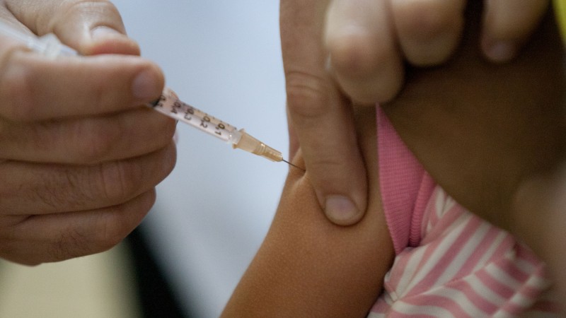 Menina toma vacina no braço. 