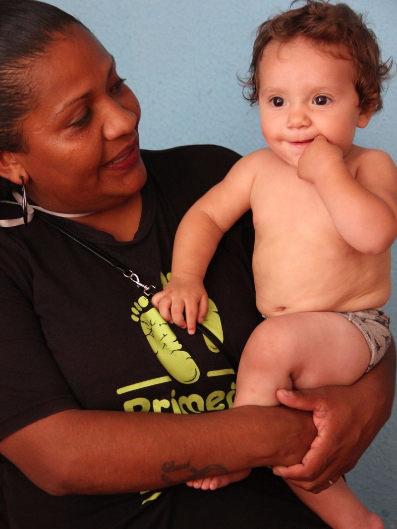 A visitadora do PIM Lucélia da Rosa segura o bebê Davi Luiz no colo. Os dois sorriem. 