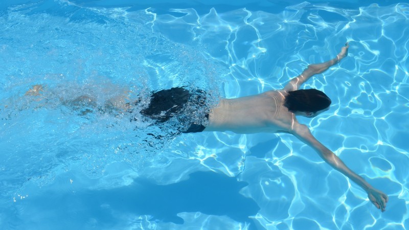 Jovem de calção mergulha em piscina